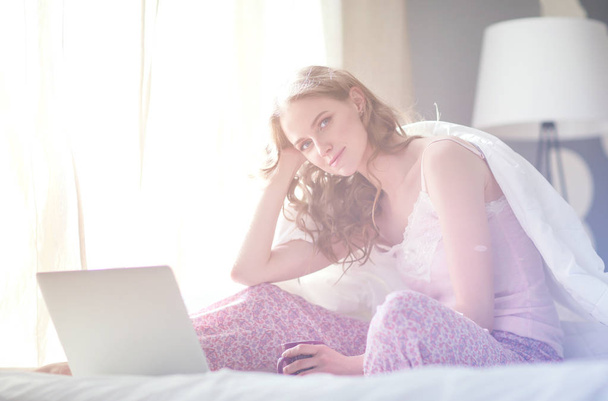 Young beautiful woman sitting in bed with laptop. - Valokuva, kuva