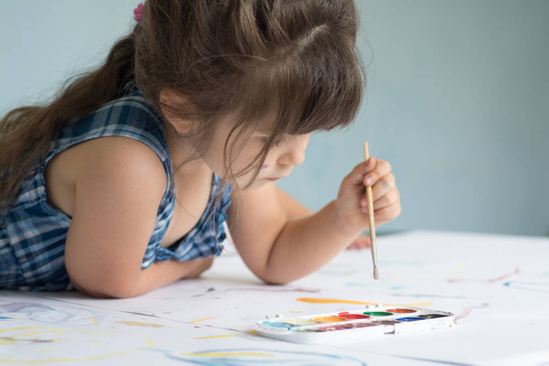Four years child is painting at home. Beautiful little girl with paint brush and watercolor. - Photo, Image