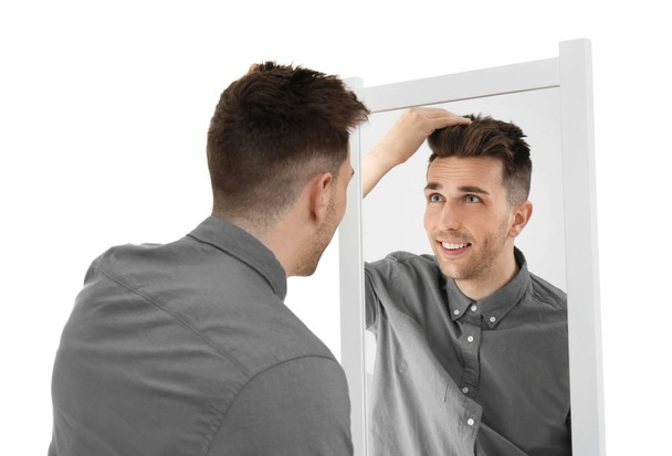Young man looking at himself in mirror on white background - Foto, Imagen