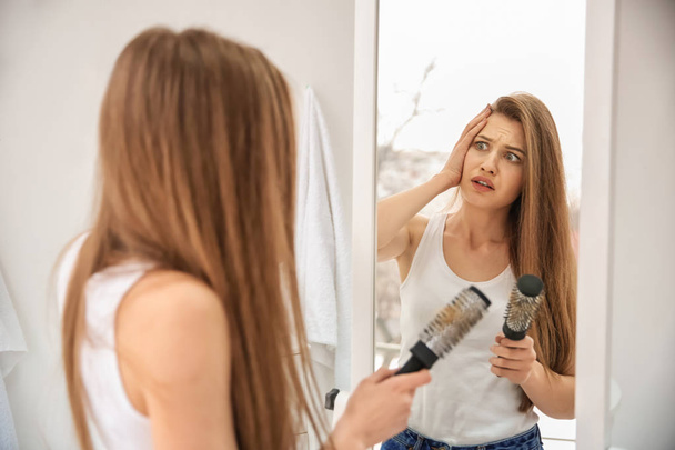 Young woman with hair loss problem looking in mirror indoors - Fotó, kép