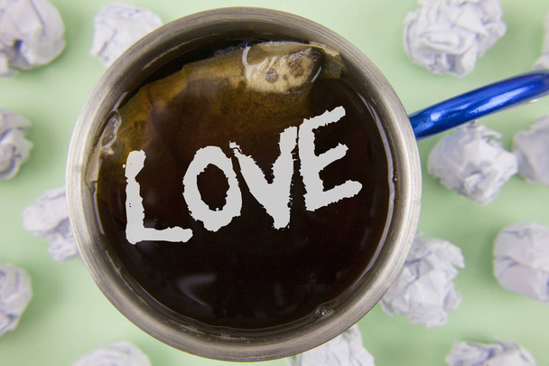 Text sign showing Love. Conceptual photo Intense feeling Deep affection Romantic Sexual attachment Relationship written on Black Tea in Cup within Crumpled Paper Balls on plain Green background. - Photo, Image