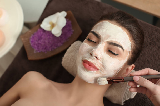 Cosmetologist εφαρμογή μάσκας στο πρόσωπο της νεαρής γυναίκας στο σαλόνι σπα - Φωτογραφία, εικόνα