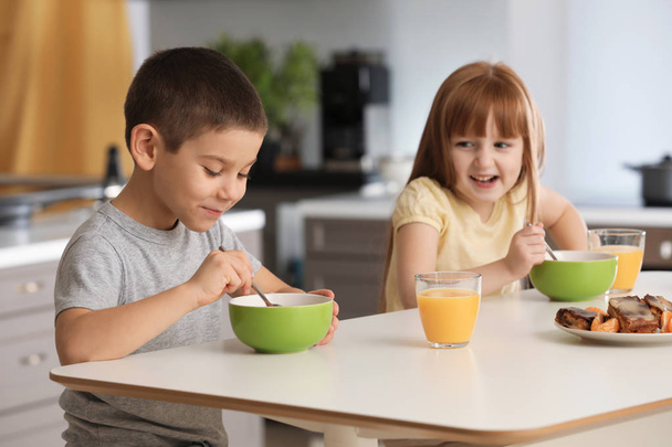 Niños pequeños y divertidos desayunando y bebiendo jugo de cítricos en casa
 - Foto, Imagen