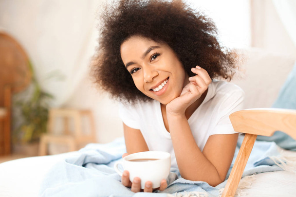Bella donna afro-americana che beve tè sul letto
 - Foto, immagini