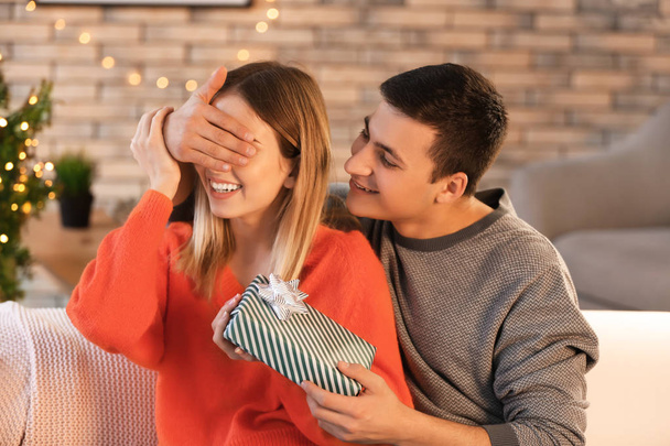 Young man giving Christmas present to his beloved girlfriend at home - Photo, Image