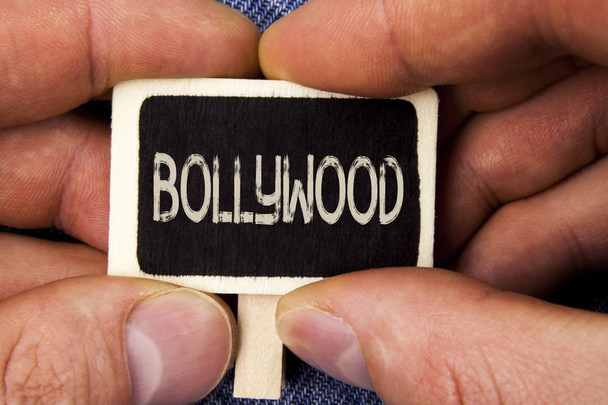A escrever um bilhete a mostrar Bollywood. Foto de negócios mostrando cinema indiano uma fonte de entretenimento escrito em Pedaço de madeira segurando por homem no fundo Blue Jeans
. - Foto, Imagem