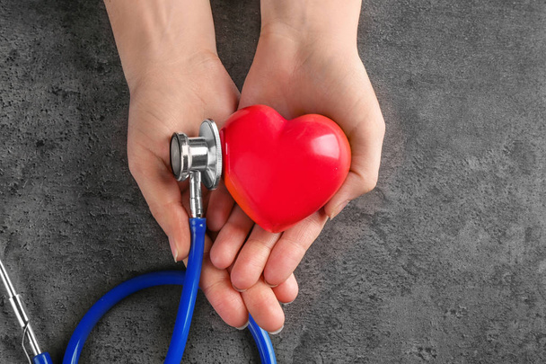 Mani femminili con stetoscopio e piccolo cuore su sfondo grigio scuro
 - Foto, immagini