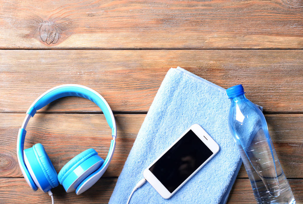 Composición plana con smartphone, botella de agua, toalla y auriculares sobre fondo de madera. Entrenamiento en el gimnasio
 - Foto, imagen
