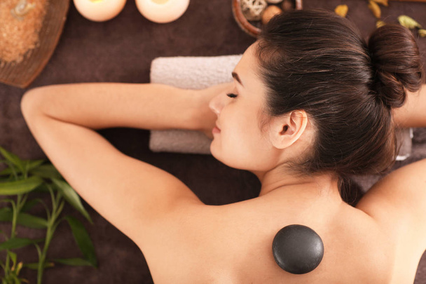 Молода жінка проходить терапію гарячим каменем на масажному столі в спа-салоні, вид зверху
 - Фото, зображення