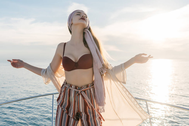 a luxurious attractive girl in a fashionable bathing suit enjoying the sun and warmth, sailing on a yacht to the islands - Foto, Imagem