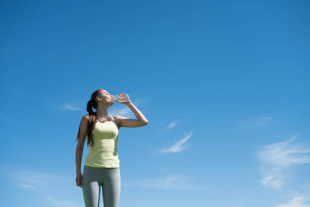 athletic young girl drinks water after a difficult long workout outdoors on a warm spring day - Foto, Imagem