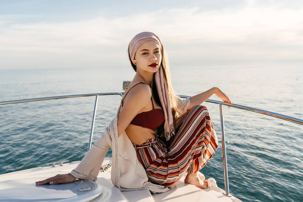 a stylish rich woman with a headscarf sitting on her white yacht in the llah of the sun, sailing to the islands - Photo, Image