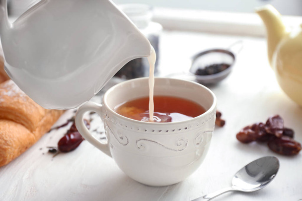 テーブルの上の香り高い紅茶とカップにミルクを注ぐ - 写真・画像