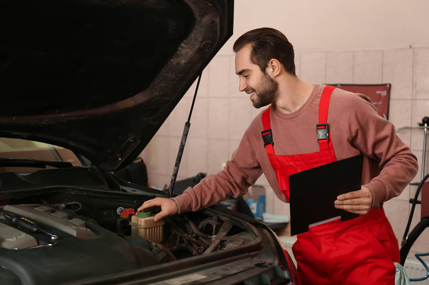 Nuori automekaanikko korjaamassa autoa huoltokeskuksessa
 - Valokuva, kuva