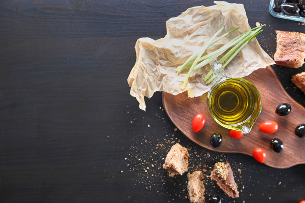 Brocca di olio, olive nere, pane e pomodorini in tavola
 - Foto, immagini