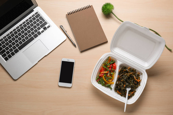 Επίπεδη lay σύνθεση με smartphone, φορητού υπολογιστή και φαγητό σε πακέτο γεύματος σε ξύλινο υπόβαθρο. Διανομή φαγητού - Φωτογραφία, εικόνα