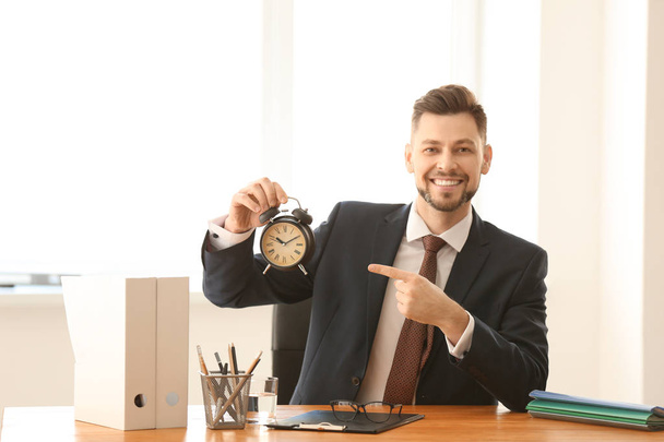 Businessman with alarm clock at table in office. Time management concept - Foto, Bild