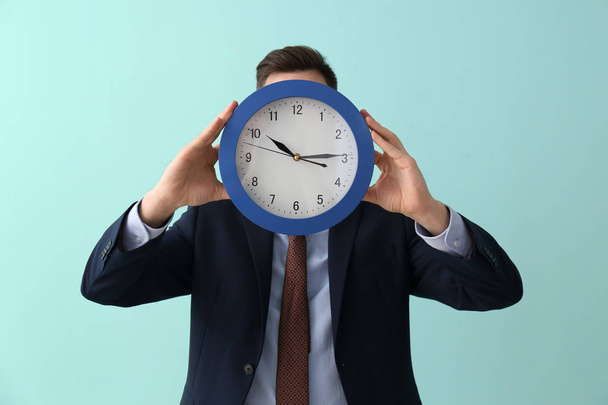 Man hiding face behind clock on color background. Time management concept - Photo, Image