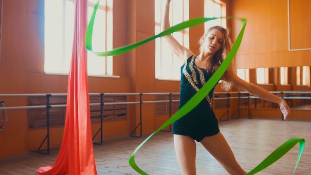 junge attraktive Frau trainiert mit grünem Band - Gymnastik im Studio mit Spiegel - Foto, Bild