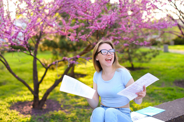 Pozitív női hallgató élvezi a tavasz park papírok olvasás. - Fotó, kép