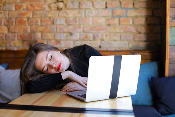 Durmiendo bastante estudiante sentado cerca de la computadora portátil moderna en la cafetería en el sofá
. - Foto, Imagen