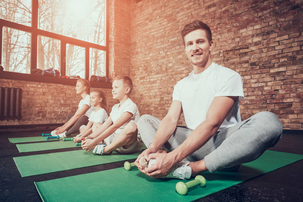 Father, mother, daughter and son sitting on green mats and stretching in gym - Foto, afbeelding