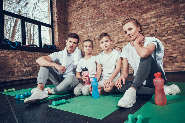 Famiglia felice seduta su tappetini verdi con bottiglie d'acqua dopo l'allenamento
  - Foto, immagini