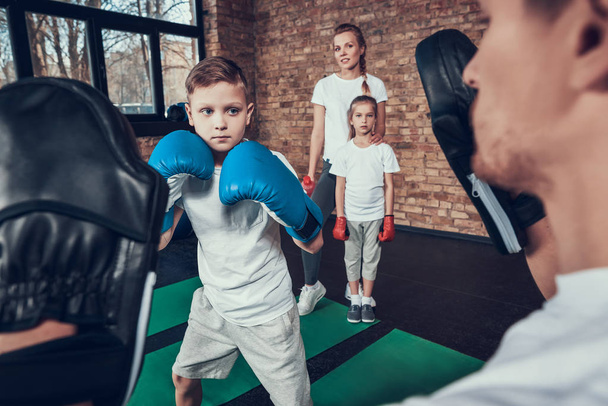 Mother and daughter looking on father teaching his son hitting boxing paws - Foto, Imagen