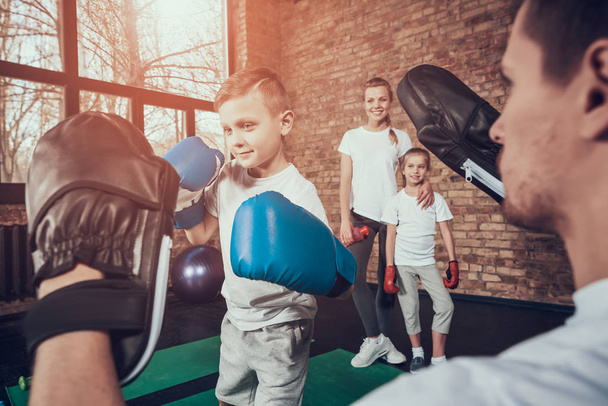 Mother and daughter looking on father teaching his son hitting boxing paws - Foto, Bild
