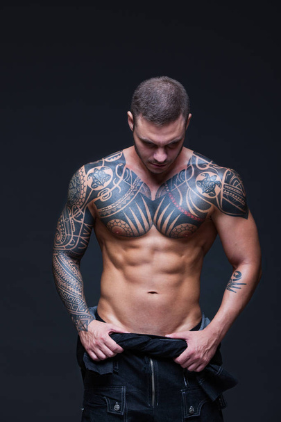 The man with a muscular naked torso with tattoos on the dark background. ABS - Foto, Imagem