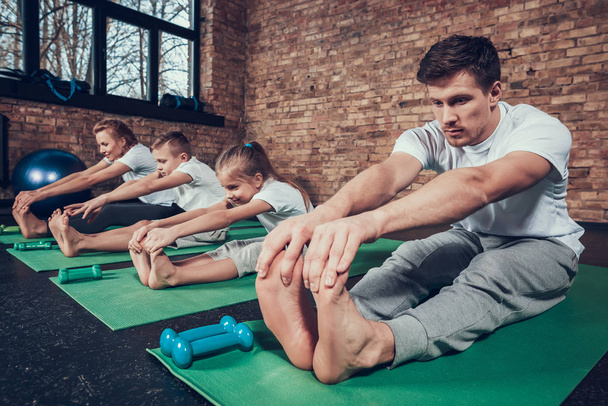 Father, mother, daughter and son sitting on green mats and stretching in gym - Fotoğraf, Görsel
