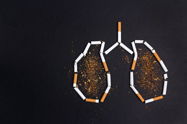 Broken cigarettes and tobacco in the form of lungs on black back - Foto, Imagen