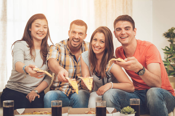 Чотири веселі друзі насолоджуються піцою разом на домашній вечірці
 - Фото, зображення