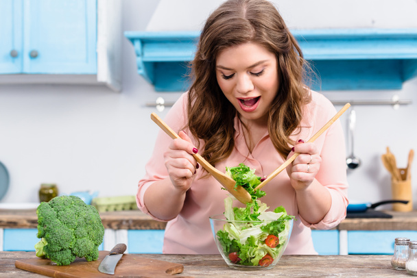 portrait de femme émotionnelle en surpoids cuisinant une salade fraîche pour le dîner dans la cuisine à la maison
 - Photo, image