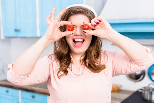 obscured view of overweight woman in headphones with cherry tomatoes in hands in kitchen - Foto, imagen
