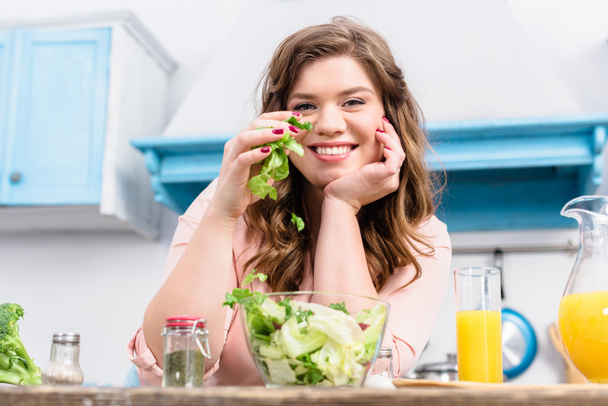 太りすぎの自宅のキッチンで新鮮なサラダとテーブルで笑顔の女性 - 写真・画像