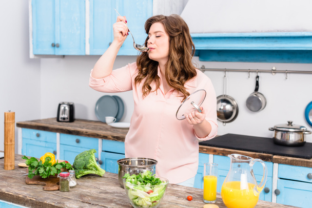 portrét mladé ženy s nadváhou vaření polévky v kuchyni doma - Fotografie, Obrázek