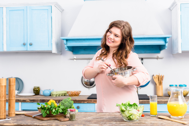 Portret van lachende overgewicht vrouw met pan staan in keuken thuis - Foto, afbeelding