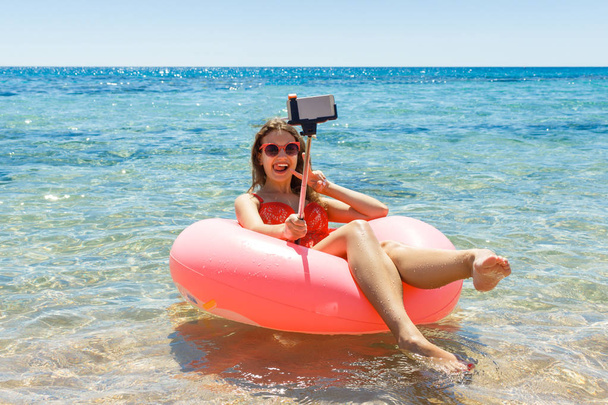 schöne junge Frau entspannt sich und macht Selfie auf aufblasbarem Donut im Meer - Foto, Bild