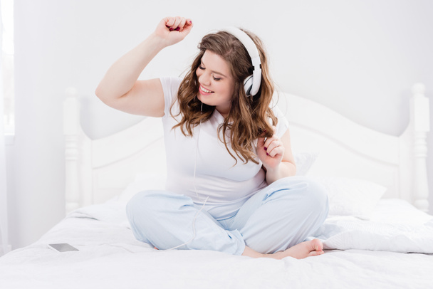 mujer sonriente en pijama escuchando música en auriculares en la cama en casa
 - Foto, imagen