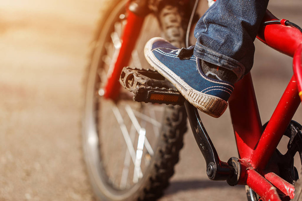 Detail of child cyclist feet riding bike on outdoor in sunny road. Closeup on pedal and foot - Фото, зображення