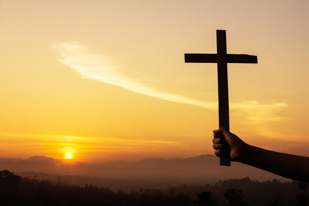 Uma mão humana segurando um crucifixo tem um nascer do sol como pano de fundo
.,  - Foto, Imagem