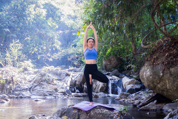 Woman meditating doing yoga on a river rock. - Photo, Image