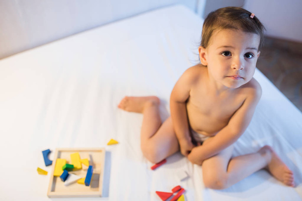 View from above of beautiful toddler girl sitting on the bed in  - 写真・画像