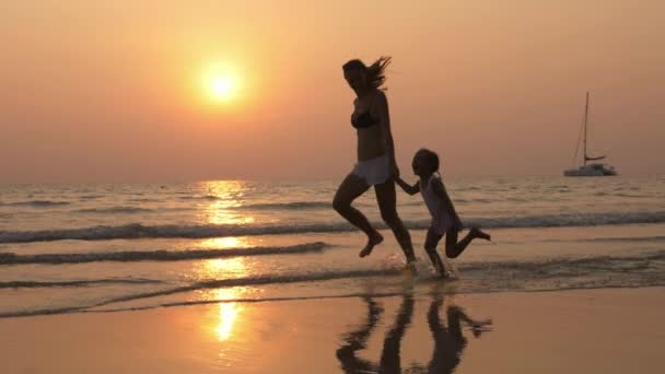 Silhouetteother z małą córeczkę uruchomiona na brzegu morza z trzymając się za ręce. - Materiał filmowy, wideo