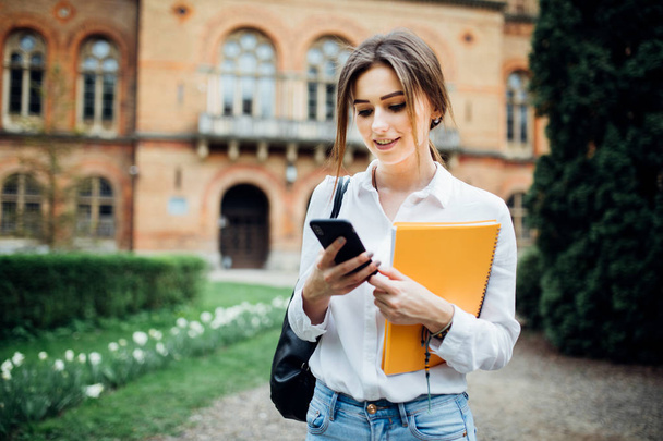 Öğrenci kız smartphone kampüs içinde açık bir şey okumak - Fotoğraf, Görsel