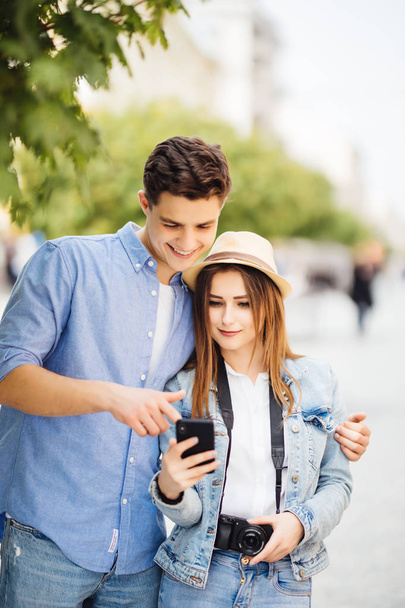 Gelukkige jonge paar kijken scherm van de telefoon op app van toeristen attracties in de straat - Foto, afbeelding