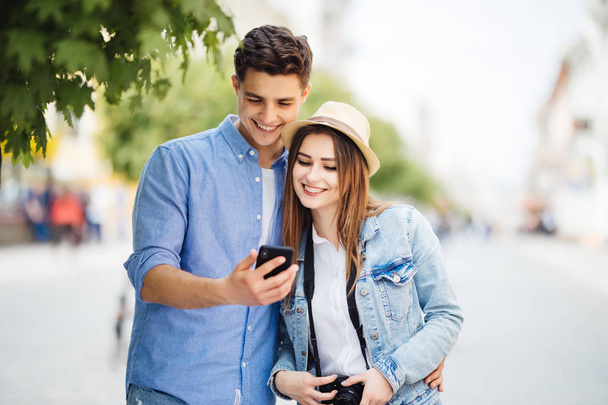 Happy young couple look at phone screen to app of tourists sightseeing in the street - 写真・画像