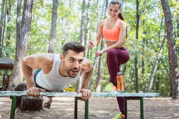 Sportieve man doen push-up in een outdoor sportschool, zijn vriendin is naar hem te kijken  - Foto, afbeelding