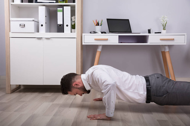 Young Businessman Doing Push Up At His Workplace - Фото, изображение